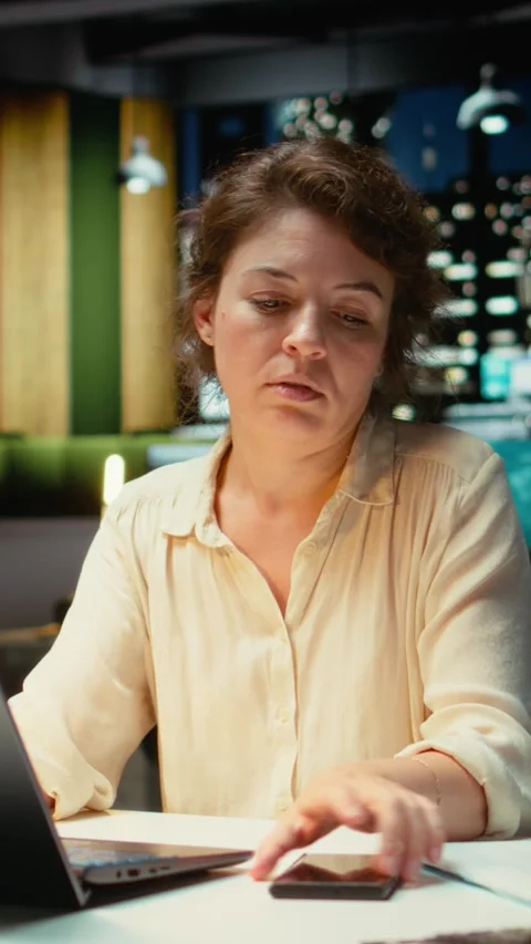 Vertical Video Female employee checking the time on her phone and closing laptop Stock Footage 317584023