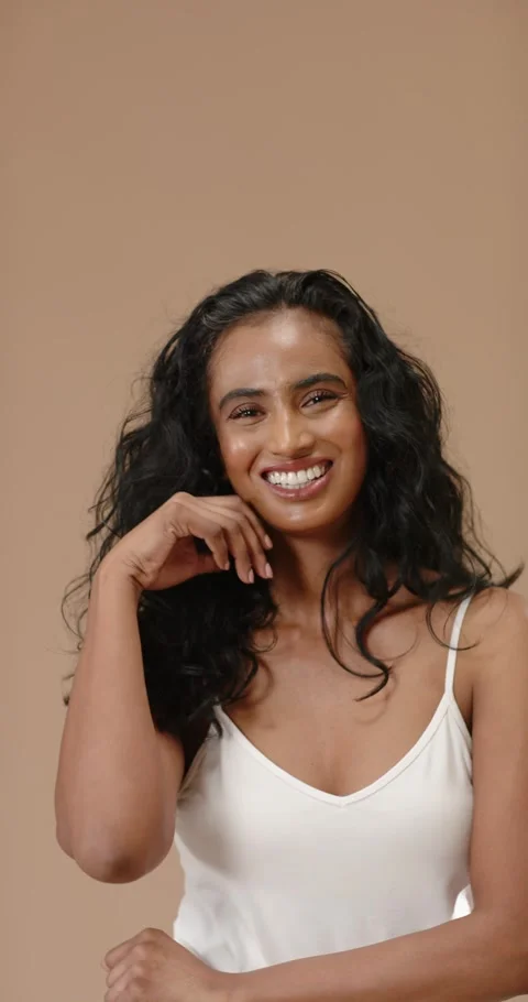 Vertical video: Female model posing for camera, smiling, flipping hair in beige Video stock 345093278