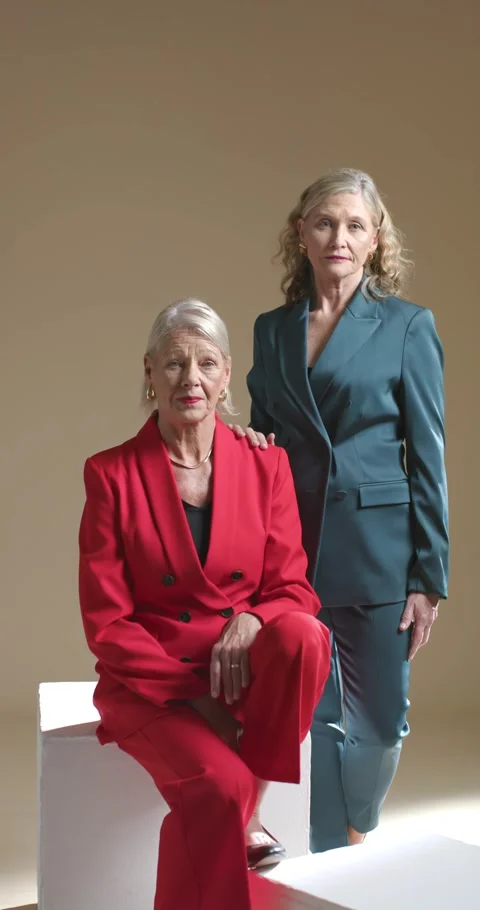 Vertical video: Female models posing in studio on cube wearing red teal suits Stock Footage 344695222
