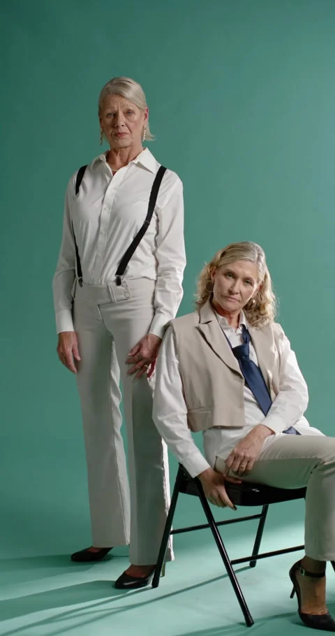 Vertical video: Female models posing during shoot on teal backdrop, seated Stock Footage 345093538