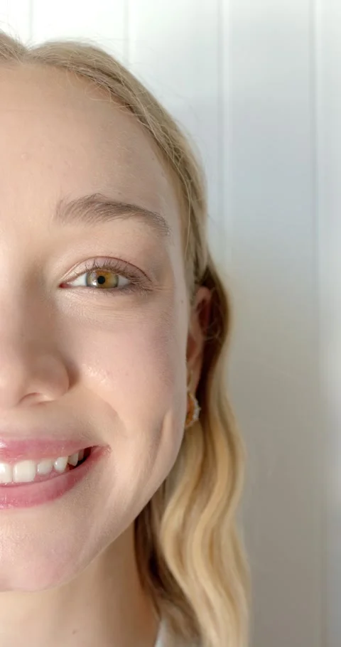 Vertical video: Female opening left eye, smiling into white wall showing gold Stock Footage 345323345