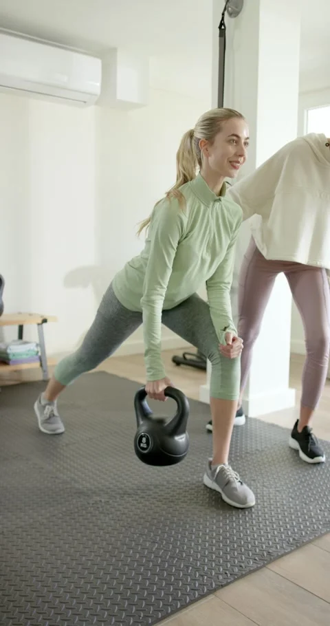 Vertical video: Female trainee and coach stepping on mat lifting kettlebell Stock Footage 346723899