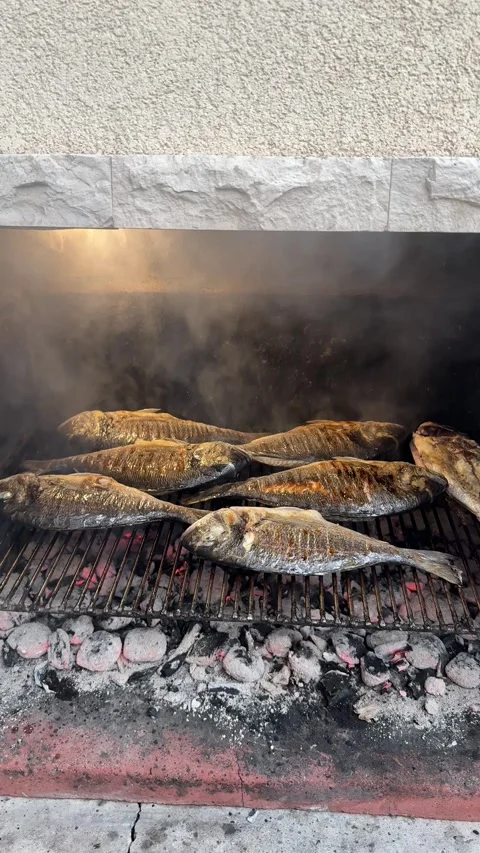Vertical video of fish grilling over fire in traditional outdoor cooking scene Video stock 319353531