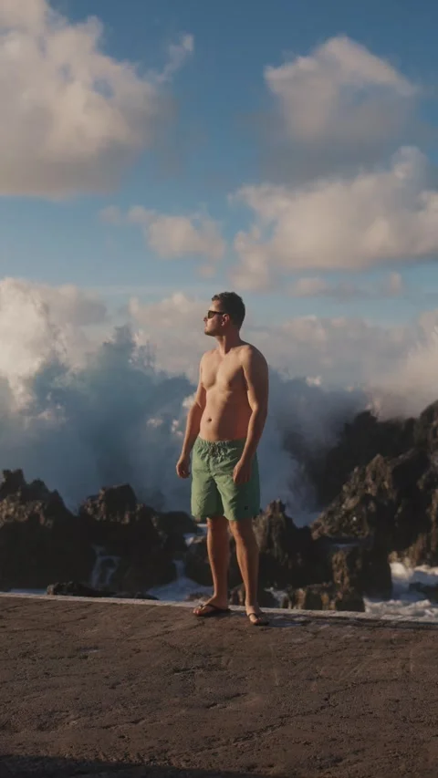 Vertical video of fit man looking at the waves as they splash in the ocean Stock Footage 299960165
