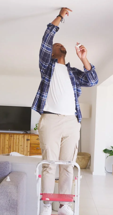 Vertical video: Fixing light after removing cover, man in plaid on ladder at Video stock 345322726