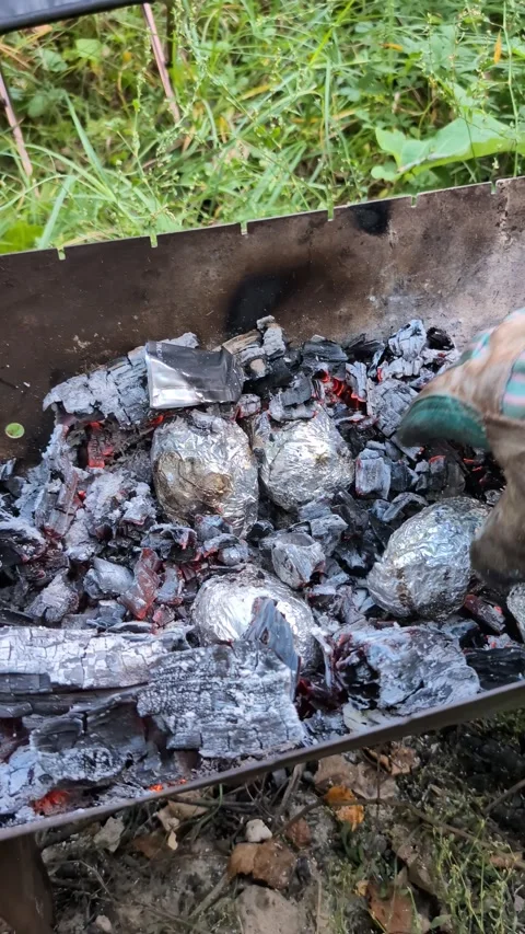 Vertical video of foil wrapped potatoes baking in hot coals on outdoor barbec Stock Footage 329173799