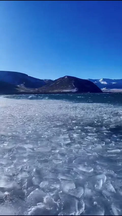 Vertical video of fragmented drift ice and slush bobbing on waves in blue mo Stock Footage 327689326