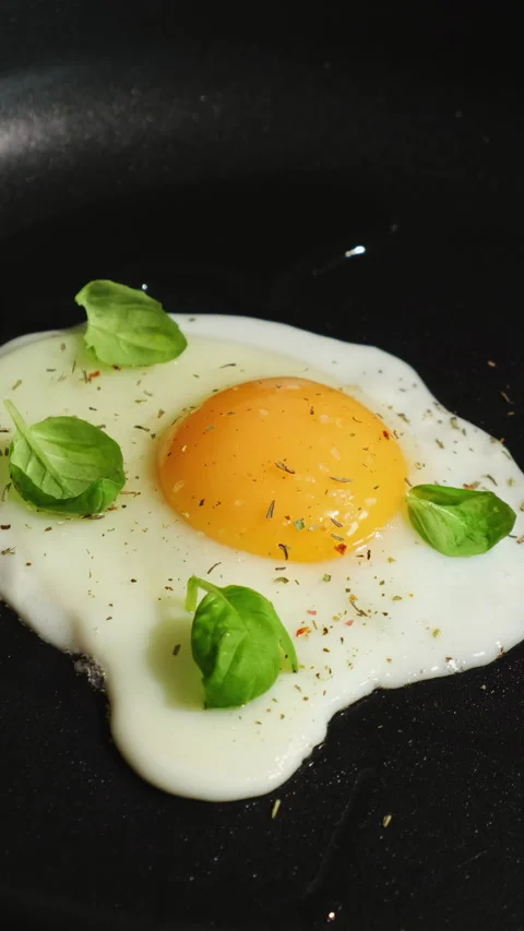 Vertical video. Fried egg sprinkled with spices and fresh basil leaves frie.. Stock Footage 340333718