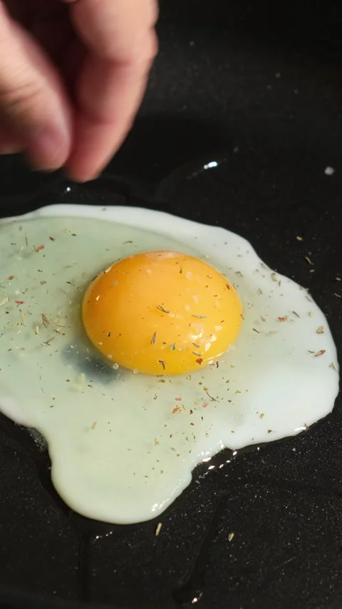 Vertical video. Fried eggs are cooked in frying pan. Female hands sprinkle .. Stock Footage 340333719