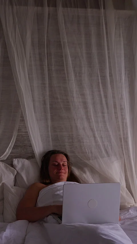Vertical video. Front View of Woman Relaxing in Large Bed While Using Laptop Ben Stock Footage 336716301