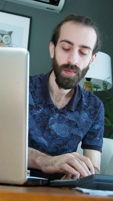 Vertical video. A frustrated man sits in front of his laptop, holding his h.. Video stock 296891006