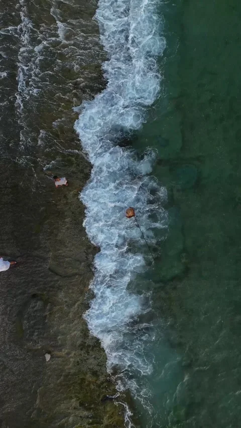Vertical Video: Gentle Waves and Fishermen on the Shore Casting Lines into the Stock Footage 297715280