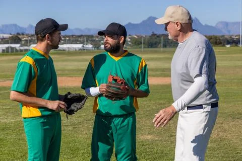 Vertical video: Gesturing coach instructing two uniformed players on baseball Stock Photos