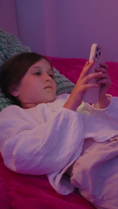 Vertical Video of Girl Lying in Bed and Using Smartphone with Neon Light Stock Footage 345528439