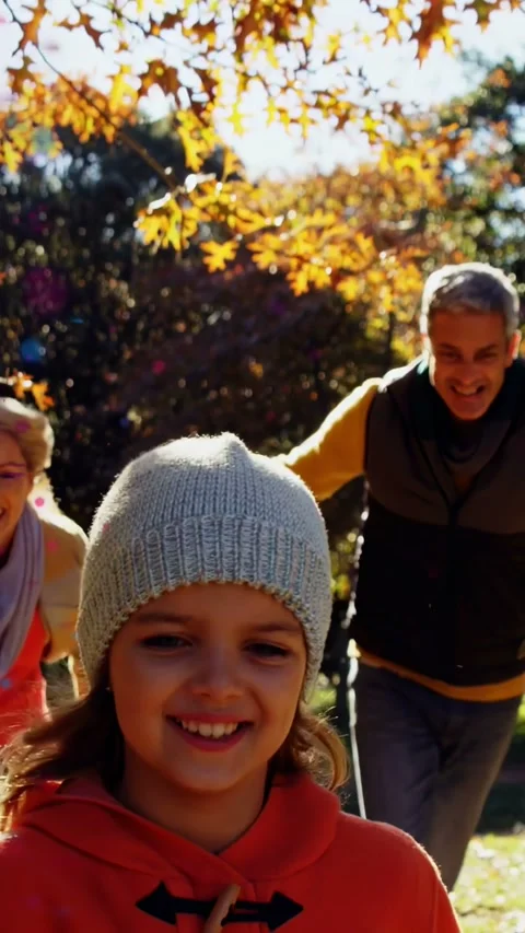 Vertical video: Girl running to lens, parents chasing, reaching, leaves adding Stock Footage 334046856