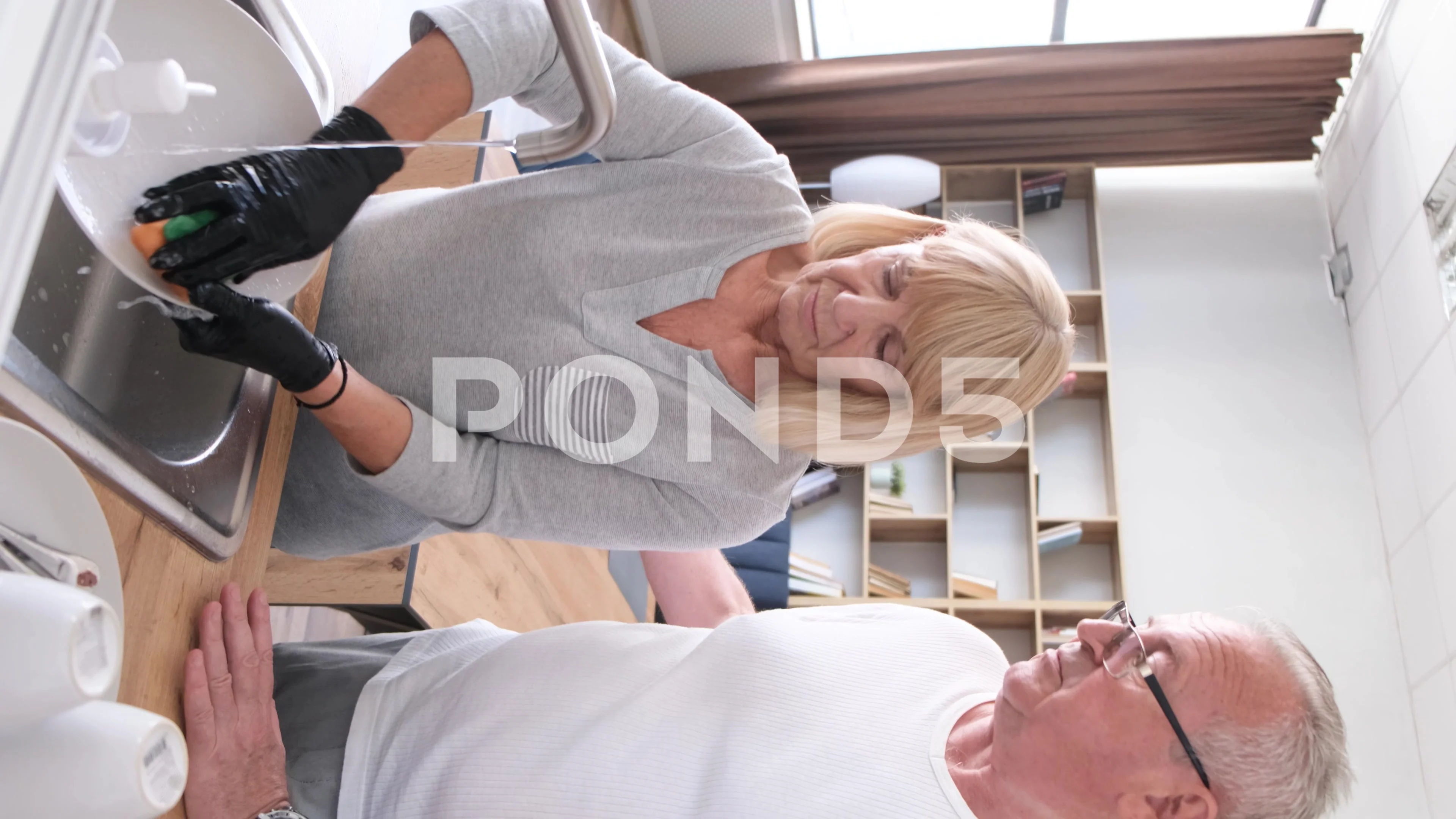 Vertical video, grandfather and grandmother wash dishes in the kitchen.  Happy