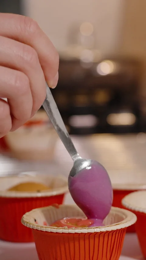 Vertical video. Hand Applying Purple Icing from Spoon to Cupcake in Red Wrapper Stock Footage 308209186
