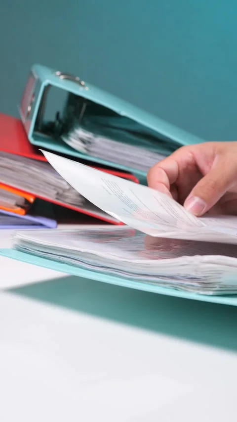 Vertical video hand browsing through paperwork filed in an open ring binder Stock Footage 342772219
