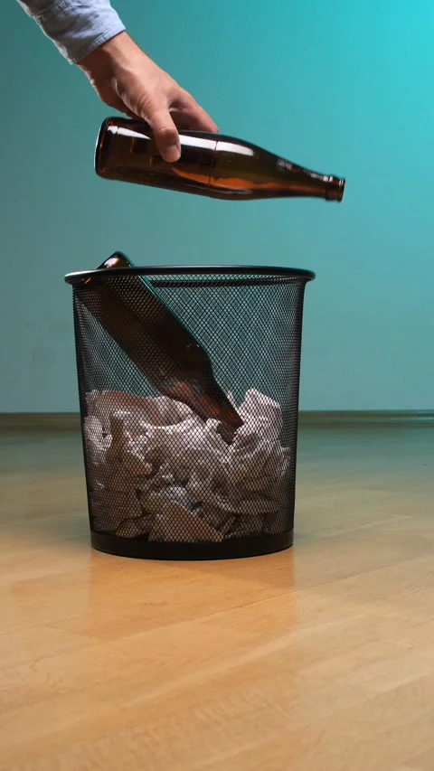 Vertical video hand dropping empty brown glass bottle into a black mesh waste Stock Footage 342761390