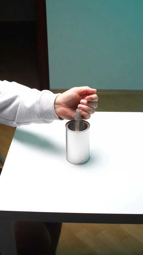 Vertical video hand holding a coin, carefully dropping it into a simple metal Stock Footage 345169956