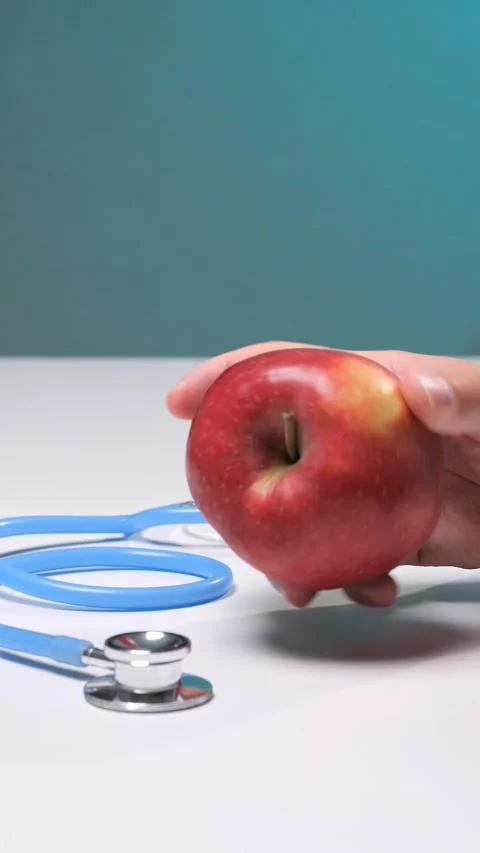 Vertical video hand holding a crisp red apple over a blue stethoscope Stock Footage 342768371