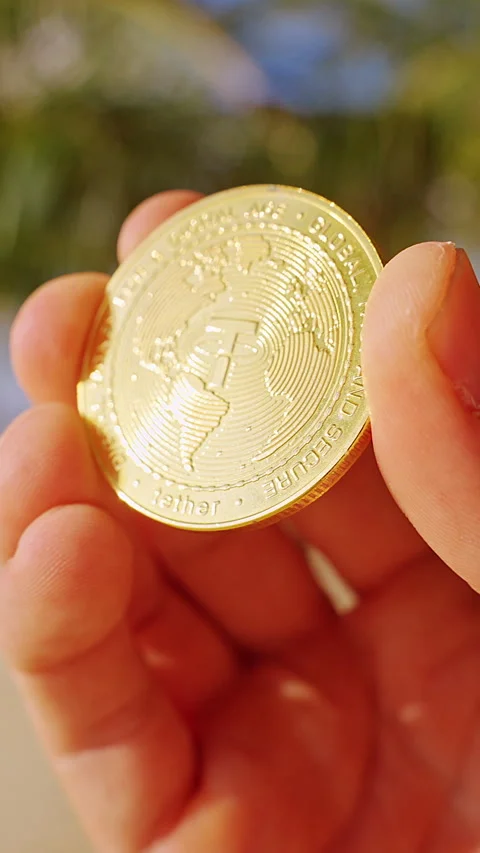 Vertical video. A Hand Holds a Gold Tether USDT Token Over a Sunlit Tropical Bea Stock Footage 327419406