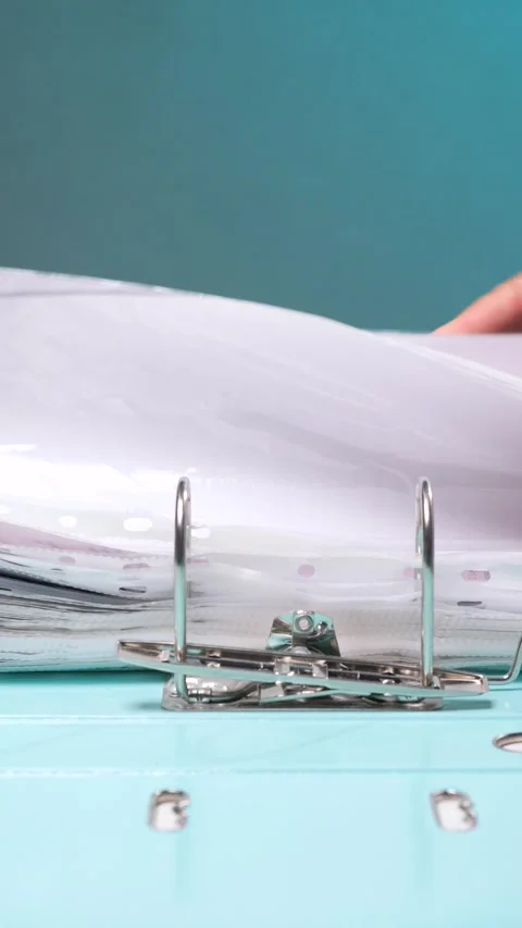 Vertical video hand placing sheets of paper into a mint green lever arch file Stock Footage 342766388