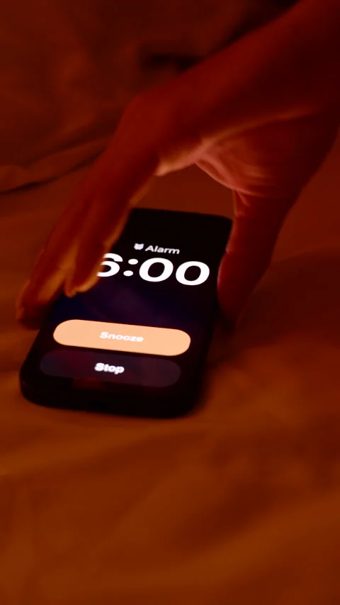 Vertical video. Hand Reaching Toward Smartphone Screen Showing 6 AM Alarm on Bed Stock Footage 319249376