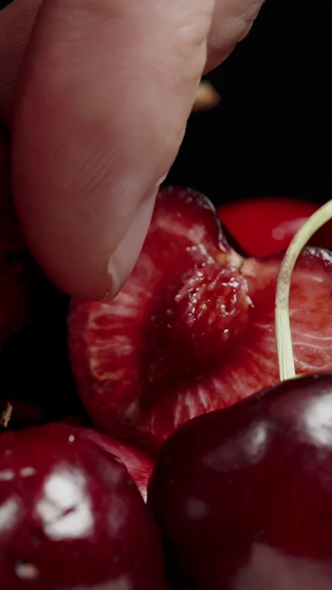 Vertical video. Hand Squeezing Juice from Cherry Half, Berries on Black Stock Footage 278317962