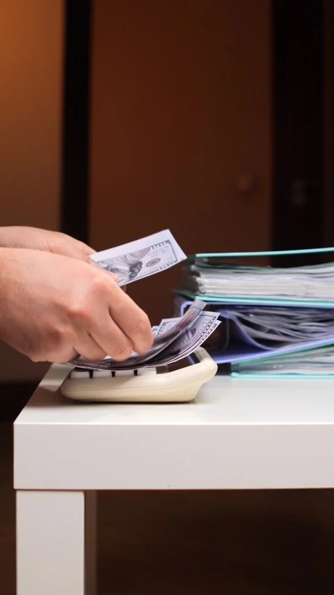 Vertical video hands are counting a stack of us 100 dollar bills, placing them Stock Footage 347236535
