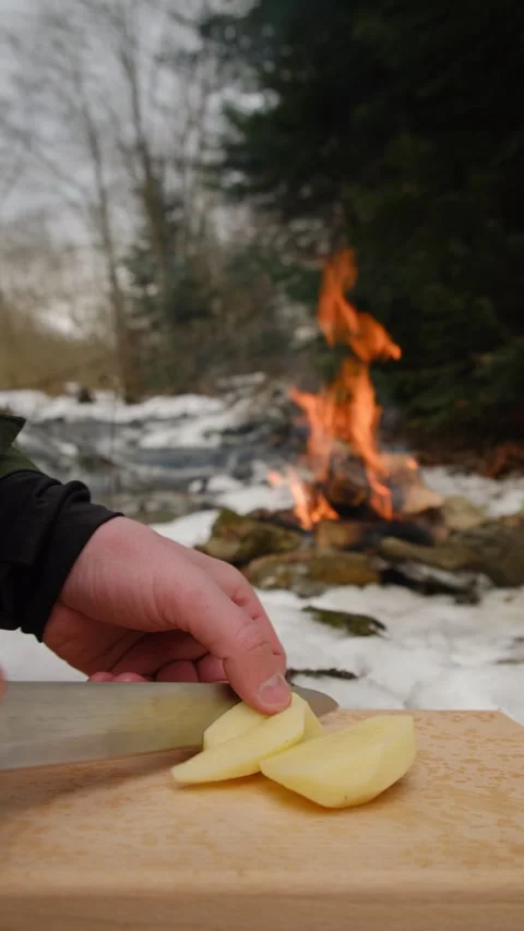 Vertical video of hands chopping potato on wooden board on background bonfire Stock Footage 297964271