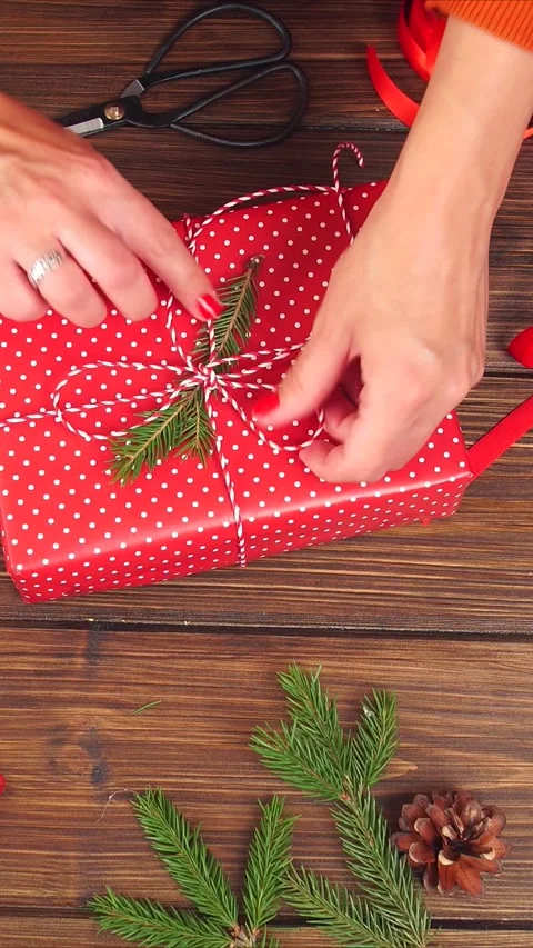 Vertical video of Hands wrapping red polka dot gift on wooden table with ribbon Stock Footage 322508311