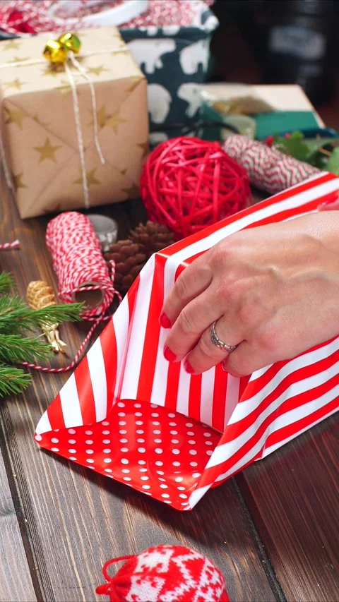 Vertical video of hands wrapping striped gift paper on table; close-up of woman Stock Footage 322508240