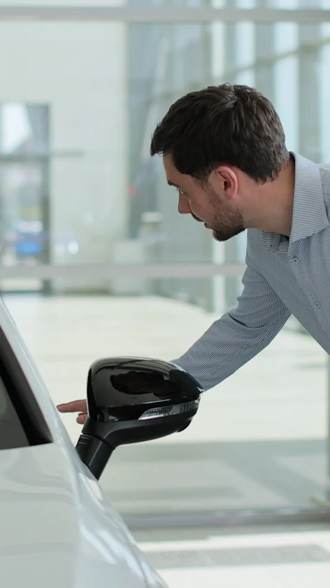 Vertical video Handsome man touching new car in showroom. Видео 337239610