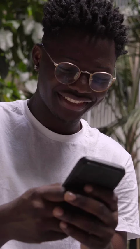 Vertical video of a happy black man using a cell phone and looking camera on Stock Footage 243940909