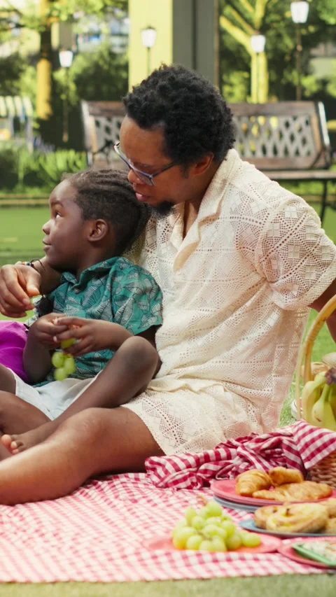 Vertical Video Happy boy shares grapes with parents relaxing on checkered Stock Footage 341471153