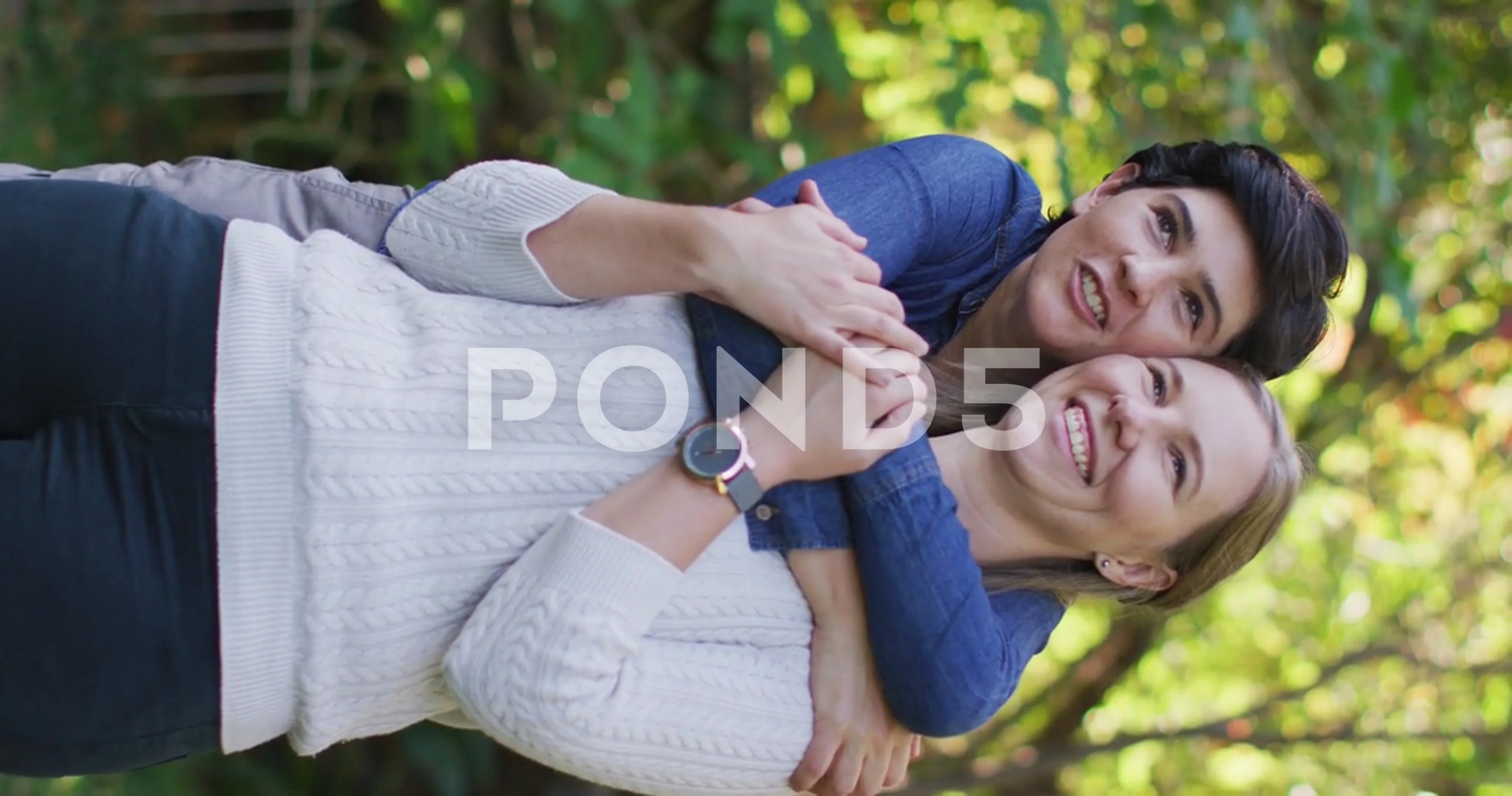 Vertical video of happy caucasian lesbian couple embracing in garden