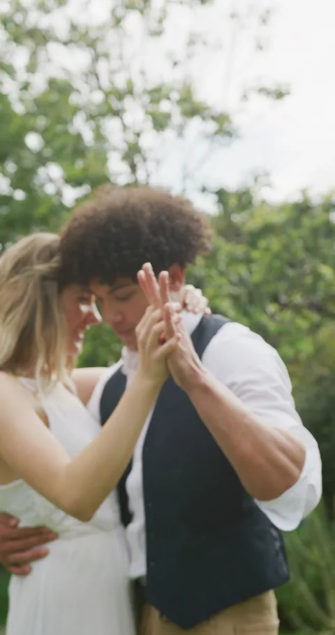 Vertical video of happy diverse couple dancing in garden on sunny day at wedding Stock Footage 346720882
