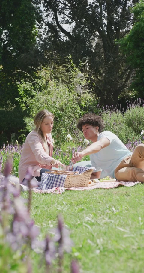 Vertical video of happy diverse couple having picnic in garden on sunny day Stock Footage 346723294