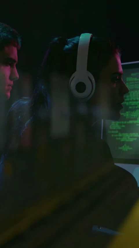 Vertical video: Headset coder and man watching screen, bokeh shifting green code Stock Footage 332594637