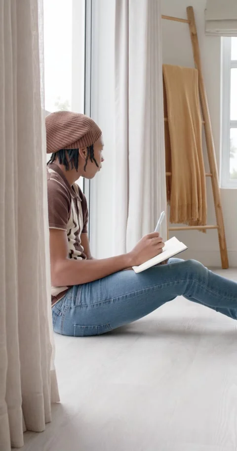 Vertical video: Holding pen and notebook, man with beanie sitting by glass door Stock Footage 343000318