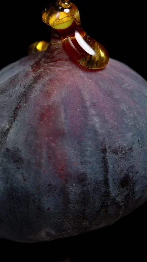 Vertical video. Honey flows in a thin stream onto the rotating fig on a black ba Stock Footage 253567948