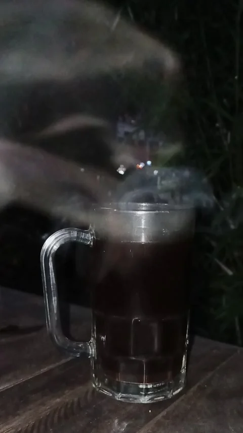 Vertical video of Hot steaming black coffee in a clear glass mug outdoors at Stock Footage 341675623
