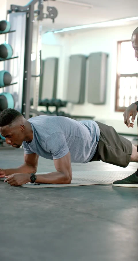 Vertical video: Inside fitness studio, man propping into plank while trainer Stock Footage 345320221