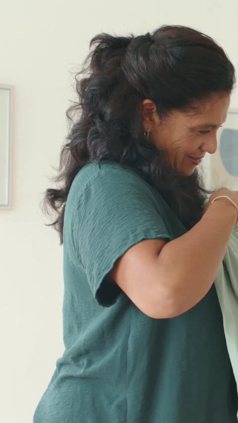 Vertical video: Inspecting woman adjusting light green garment at home in teal Stock Footage 348491237