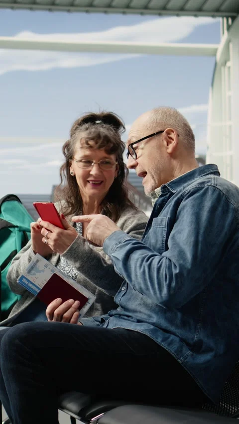 Vertical Video Joyful elderly man and woman using mobile phone in airport lounge Stock Footage 344373430