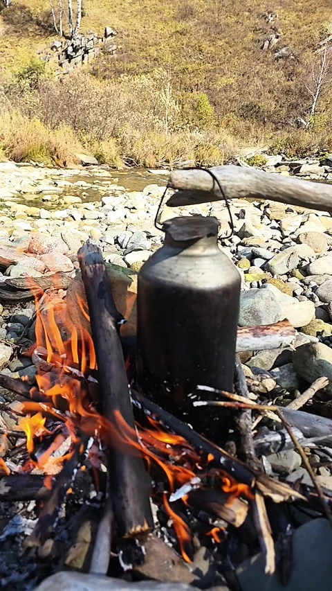 Vertical Video of a Kettle Boiling Over a Campfire by a River Stock Footage 348245284