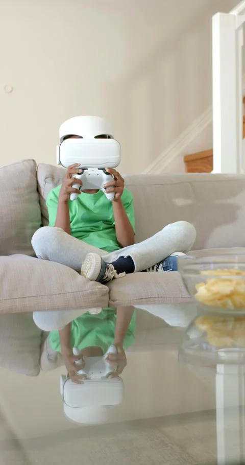 Vertical video: Kid is sitting on couch pressing controller while playing on VR Stock Footage 346600071