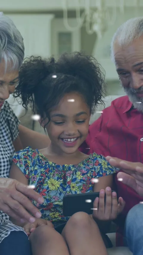 Vertical video: Kid tapping phone and waving, sparking confetti while seniors Stock Footage 334378733