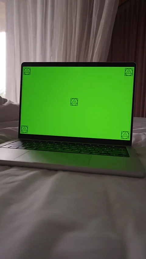 Vertical video. Laptop With Green Screen Stands on a Bed Near a Bright Window in Stock Footage 336553676